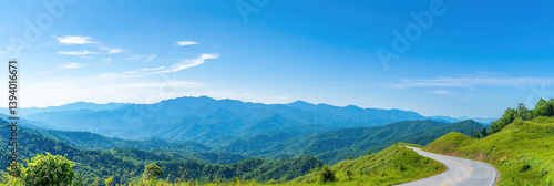 A winding mountain road leading to breathtaking panoramic views under a vibrant summer sky with lush green hillsides and a clear blue horizon.
