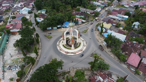 Rantau, Indonesia, 20 Desember 2024, Aerial view of city square roundabout with traffic activity and dense settlements around the roundabout