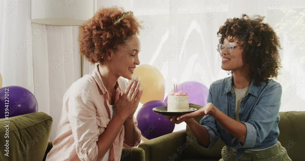 Happy diverse lesbian couple laughing and holding hands at home with colorful balloons around Happy diverse lesbian couple laughing and holding hands at home with colorful balloons around