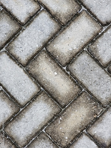 Background of a walkway or pavement with a herringbone-patterned gray tiled surface