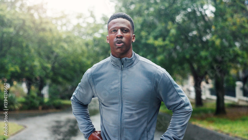 Fitness, man and tired with resting at park for running fatigue, workout recovery and cardio challenge. Runner, black person and breathing in road with marathon break, exhausted or dedication in rain
