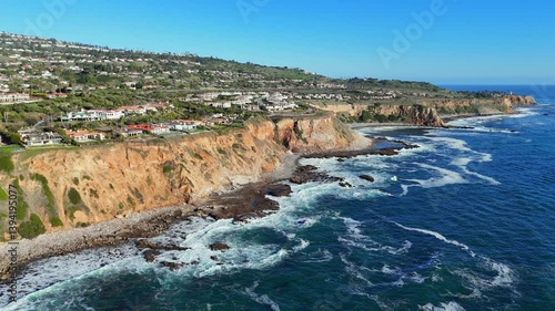 A dramatic side view of bright orange cliffs in Rancho Palos Verdes, Los Angeles, lined with luxurious homes overlooking the Pacific Ocean. Captures the unique coastal geography of California.