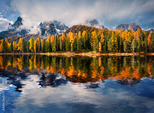 Huge peaks and colorful larch trees reflected in the calm waters of Antorno lake. Dramatic autumn scene of Dolomite Alps, National Park Tre Cime di Lavaredo, Italy. 