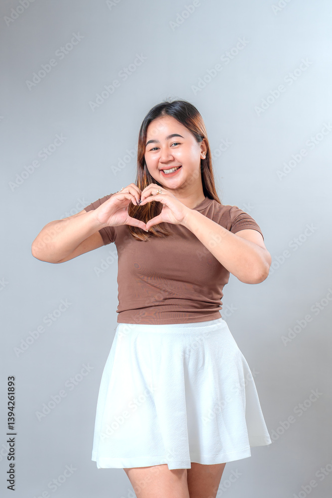 Smiling young woman making a heart shape with her hands, expressing love, kindness, and positivity. Her happy facial expression is ideal for advertising and lifestyle themes. Smiling young woman making a heart shape with her hands, expressing love, kindness, and positivity. Her happy facial expression is ideal for advertising and lifestyle themes.