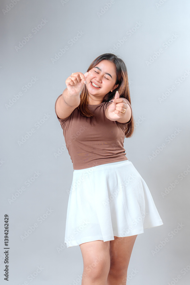 Happy young woman smiling brightly while making finger heart gesture. Her joyful and expressive facial expression shows love, positivity, and enthusiasm. Happy young woman smiling brightly while making finger heart gesture. Her joyful and expressive facial expression shows love, positivity, and enthusiasm.