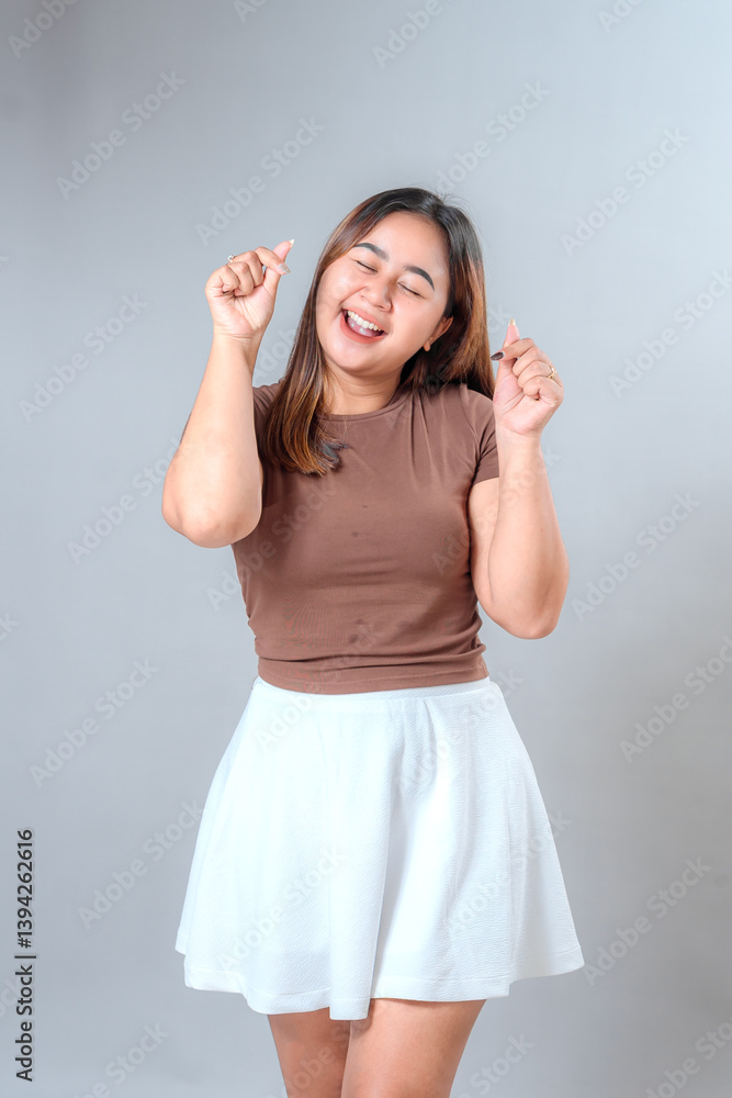 Happy young woman smiling brightly while making finger heart gesture. Her joyful and expressive facial expression shows love, positivity, and enthusiasm. Happy young woman smiling brightly while making finger heart gesture. Her joyful and expressive facial expression shows love, positivity, and enthusiasm.