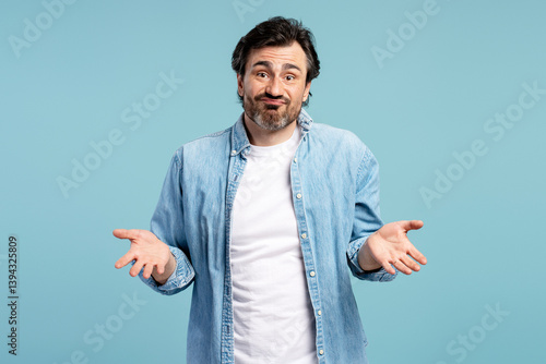 Confused man shrugging shoulders gesturing i don't know on blue background