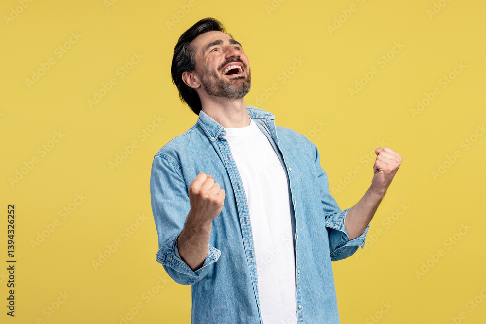 Excited man celebrating with fists raised on yellow background Excited man celebrating with fists raised on yellow background