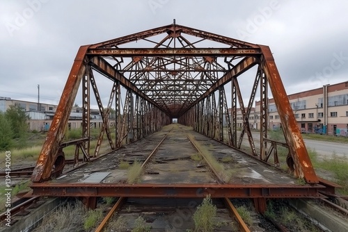 A decayed industrial bridge, its metal framework covered in rust, looming over an abandoned railway yard.