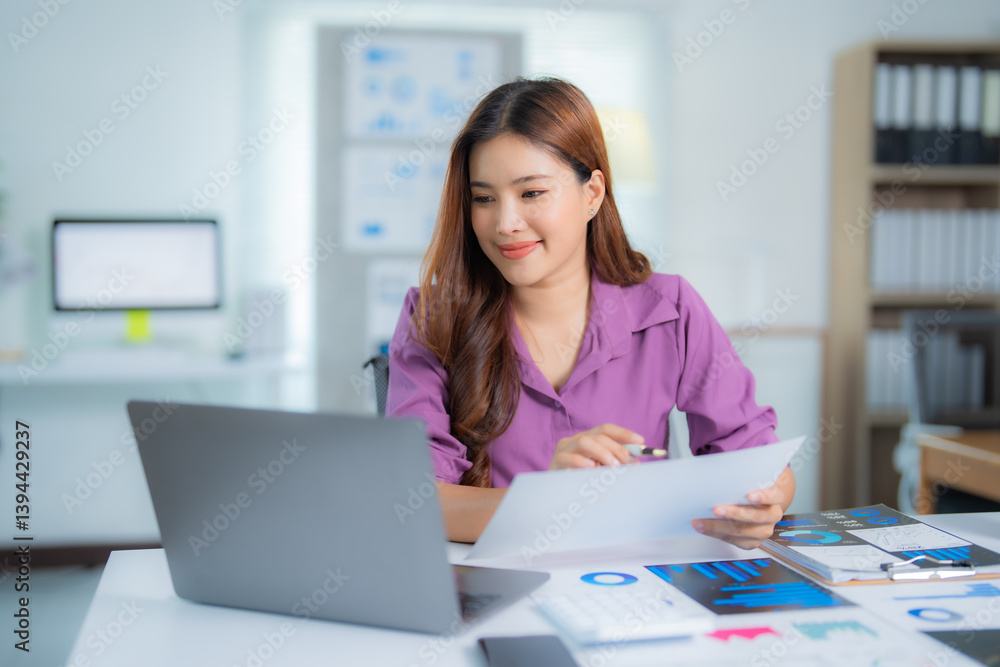 Young Asian businesswoman comparing printed documents with data on laptop, analyzing financial charts, working with marketing research graphs, planning business strategy in modern office Young Asian businesswoman comparing printed documents with data on laptop, analyzing financial charts, working with marketing research graphs, planning business strategy in modern office