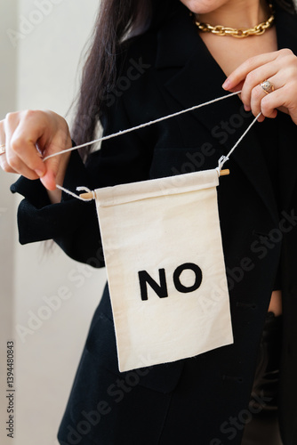 A woman in a black blazer resolutely holds a small banner reading 'NO', conveying a message of refusal or dissent