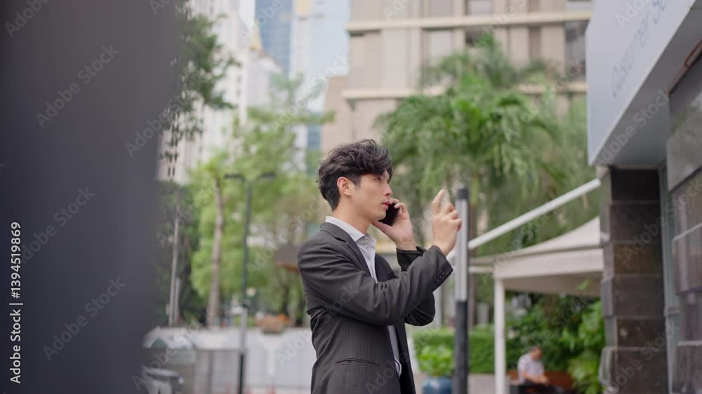 Asian young businessman talking on mobile phone while spend time in city. Asian young businessman talking on mobile phone while spend time in city.