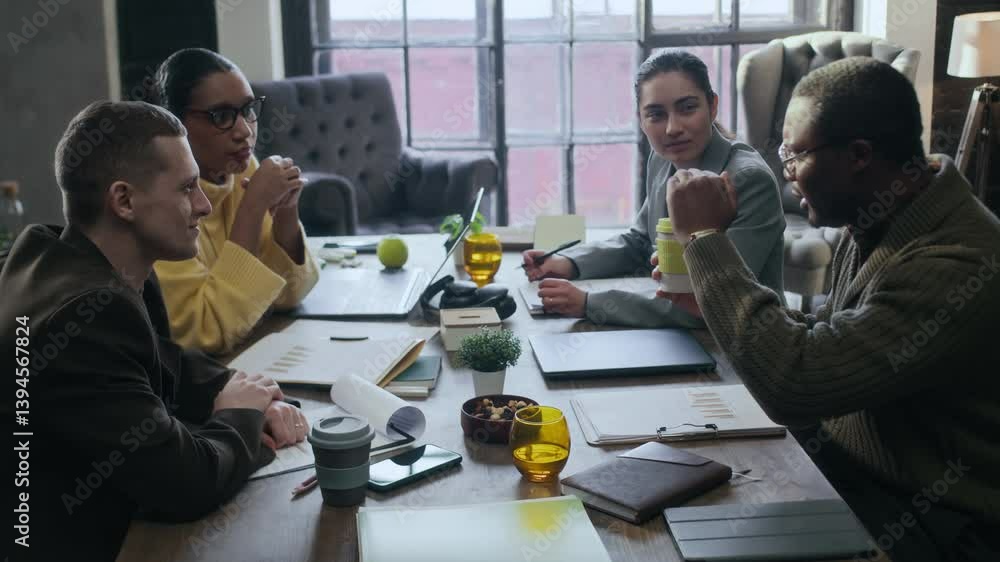 Medium shot of young inspired diverse coworking team of marketing specialists sharing ideas on product management sitting at one table in modern green office and discussing business project Medium shot of young inspired diverse coworking team of marketing specialists sharing ideas on product management sitting at one table in modern green office and discussing business project