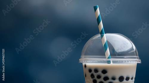 close up view of bubble tea with tapioca pearls, served in clear plastic cup with dome lid and striped straw, set against blurred blue background