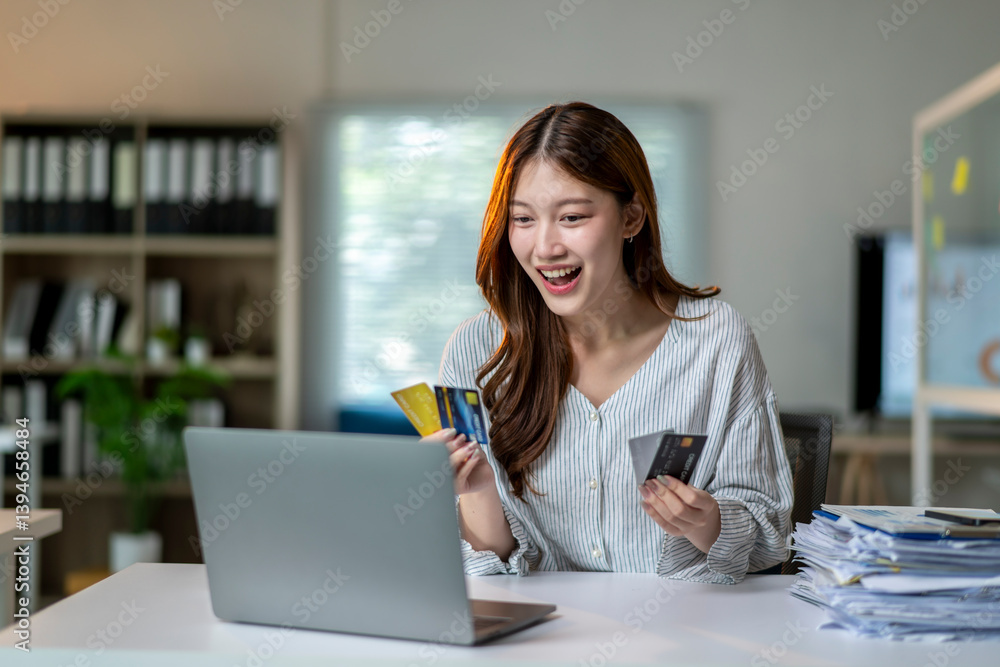 A woman is sitting at a desk with a laptop and two credit cards in her hand A woman is sitting at a desk with a laptop and two credit cards in her hand