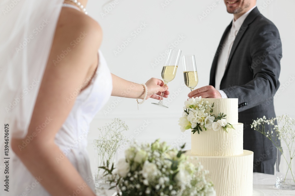 Married couple clinking glasses of champagne at table with wedding cake indoors, closeup