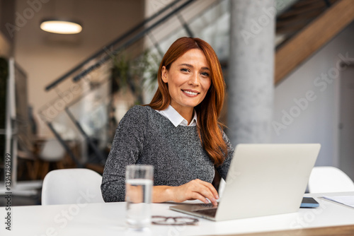 Confident Professional Woman Smiling While Working on a Laptop in Modern Office