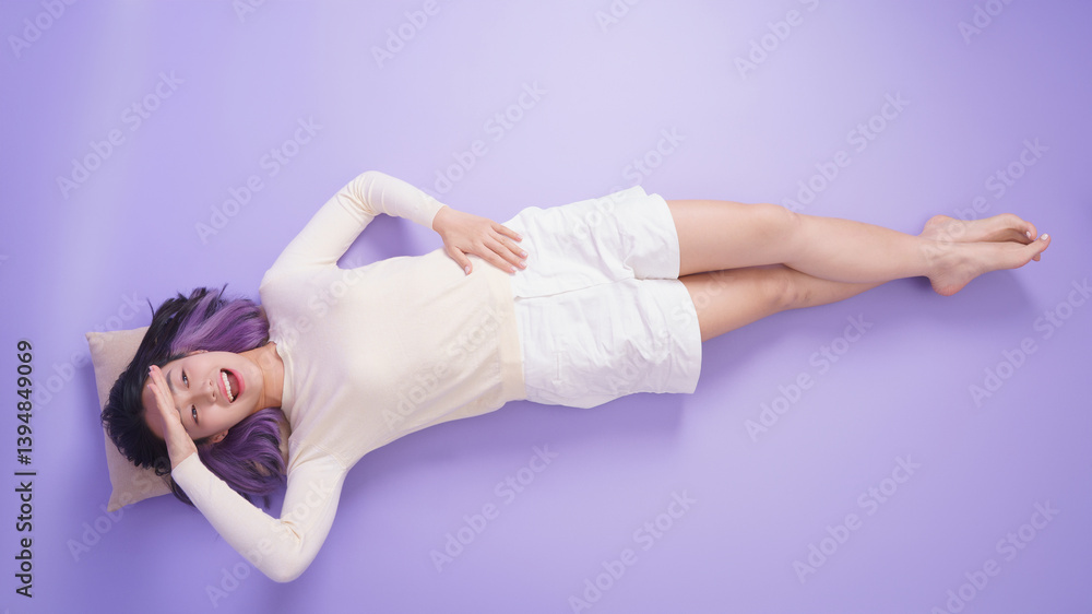 Asian woman relaxing comfortably on a purple background while resting her head on a pillow, showcasing a casual pose and soft expression Asian woman relaxing comfortably on a purple background while resting her head on a pillow, showcasing a casual pose and soft expression
