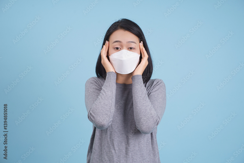 Woman wearing a face mask showing concern against a blue background while demonstrating awareness of health safety Woman wearing a face mask showing concern against a blue background while demonstrating awareness of health safety