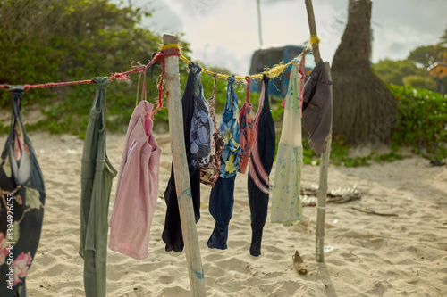 Colorful clothes hang on a rustic clothesline on a sandy beach with lush greenery and trees. Dar es Salaam, Tanzania