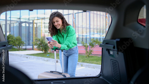Wallpaper Mural Woman loading luggage into car trunk, checking smartphone Torontodigital.ca
