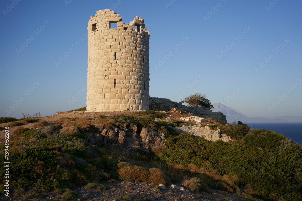 Ancient stone tower on a rugged hilltop with clear blue sky and distant mountain views. Ancient stone tower on a rugged hilltop with clear blue sky and distant mountain views.