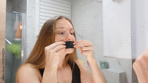 Woman with Long Brown Hair Applying Black Breathable Mouth Tape While Looking in Mirror from Front Angle in Bathroom, Anti Mouth Breathing Concept