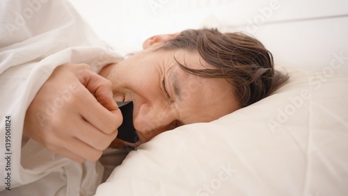 Man Pulling Off Black Mouth Tape While Lying in Bed and Grimacing in Pain, Morning Discomfort and Sleep Aid Use Concept