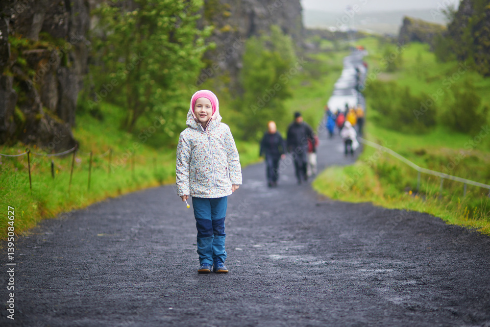 Fototapeta premium Adorable preschooler girl in Thingvellir national park in Iceland with black volcanic rocks and green plants.