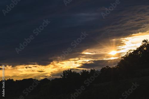 Obraz na płótnie cielo nuvoloso, coperto da grandi nuvole scure, illuminate in controluce dalla luce calda e color arancione del sole al tramonto, in estate, da un ambiente naturale di campagna w salonie
