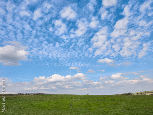Принти на полотні Verdant rolling hill rising against soft altocumulus clouds spreading across exp