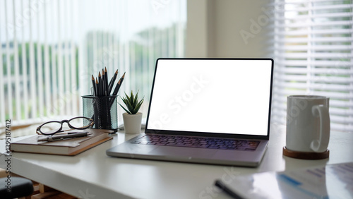 Wallpaper Mural Clean and organized desk featuring a modern laptop with a blank white screen, a coffee mug, glasses, and office supplies, with natural light coming through window blinds. Torontodigital.ca