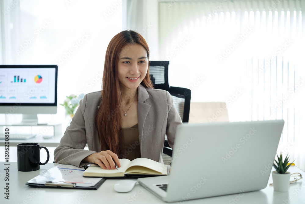 Professional businesswoman in a blazer writing in a notebook and looking at her laptop screen.