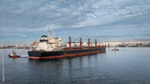 Aerial view of Tug boats assisting big cargo ship. Large cargo ship enters the port escorted by tugboats.