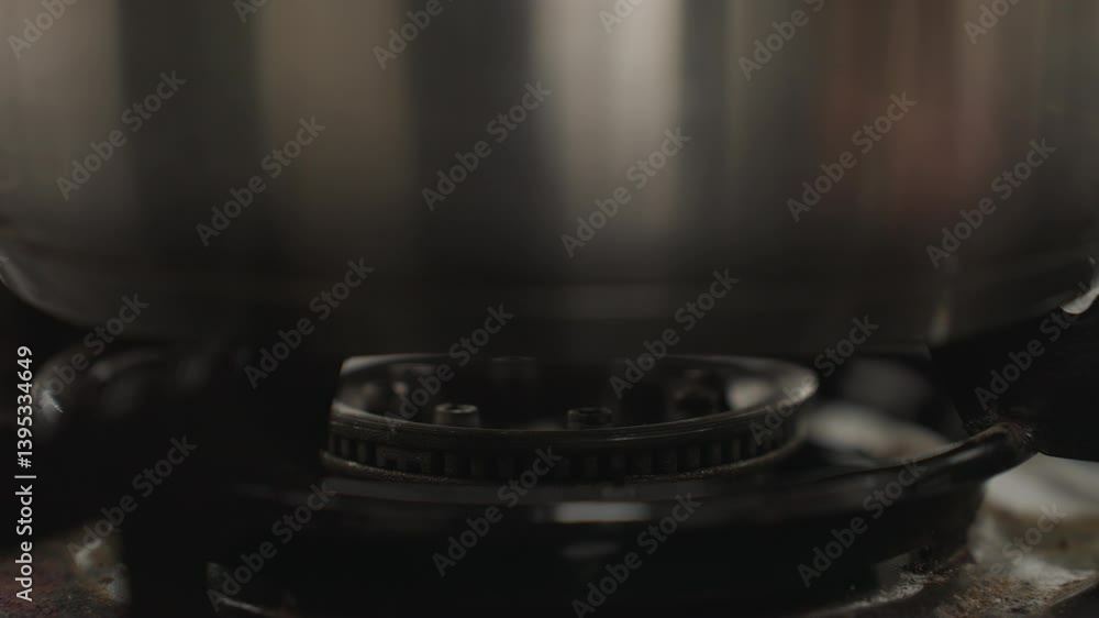 Close up of stainless steel pot placed securely on gas burner as cooking begins with flame ignited underneath, focusing on bottom of pot and burner details in a home kitchen environment Close up of stainless steel pot placed securely on gas burner as cooking begins with flame ignited underneath, focusing on bottom of pot and burner details in a home kitchen environment