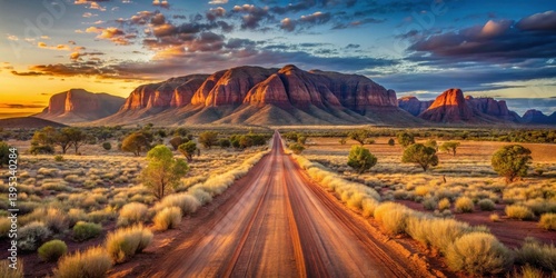 Serene Sunset Vista A Desolate Road Winds Through Golden Grasslands Towards Majestic Red Rock Formations Under a Vibrant Sky