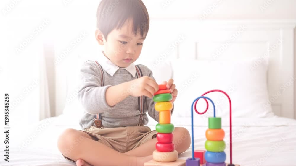 A young boy sits cross-legged on a bed, focused on stacking colorful rings and blocks A young boy sits cross-legged on a bed, focused on stacking colorful rings and blocks