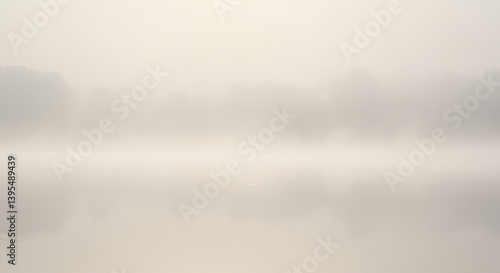 Serene misty morning over calm water reflecting distant trees in soft light