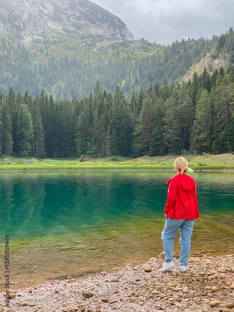 Woman in red windbreaker near the Black Lake in the Durmitor national park Woman in red windbreaker near the Black Lake in the Durmitor national park