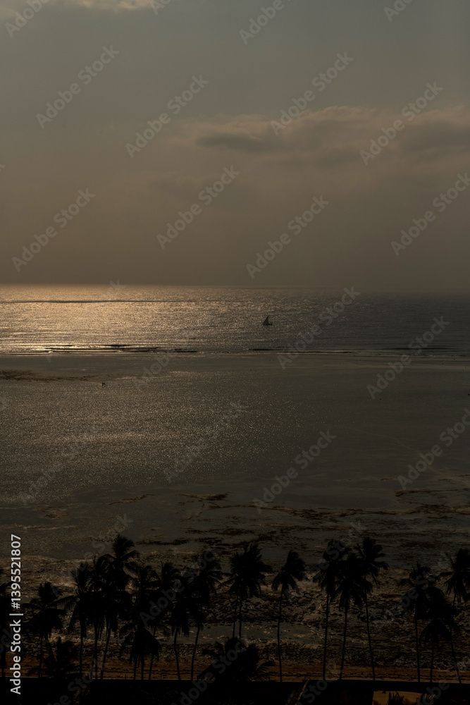 samotny, mały jacht żaglowy płynący wzdłuż rafy koralowej otaczającej lagunę, na tle wschodzącego słońca nad oceanem indyjskim, Kenia, Afryka