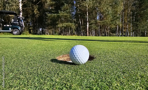 Fotografie Golf ball nearing the hole on a lush green course