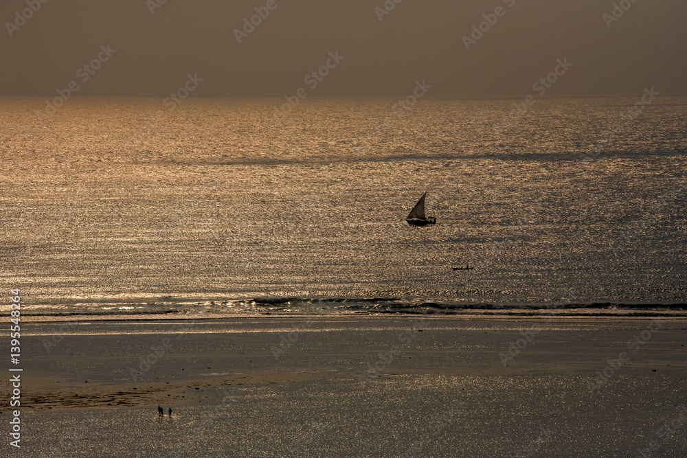 samotny, mały jacht żaglowy płynący wzdłuż rafy koralowej otaczającej lagunę, na tle wschodzącego słońca nad oceanem indyjskim, Kenia, Afryka