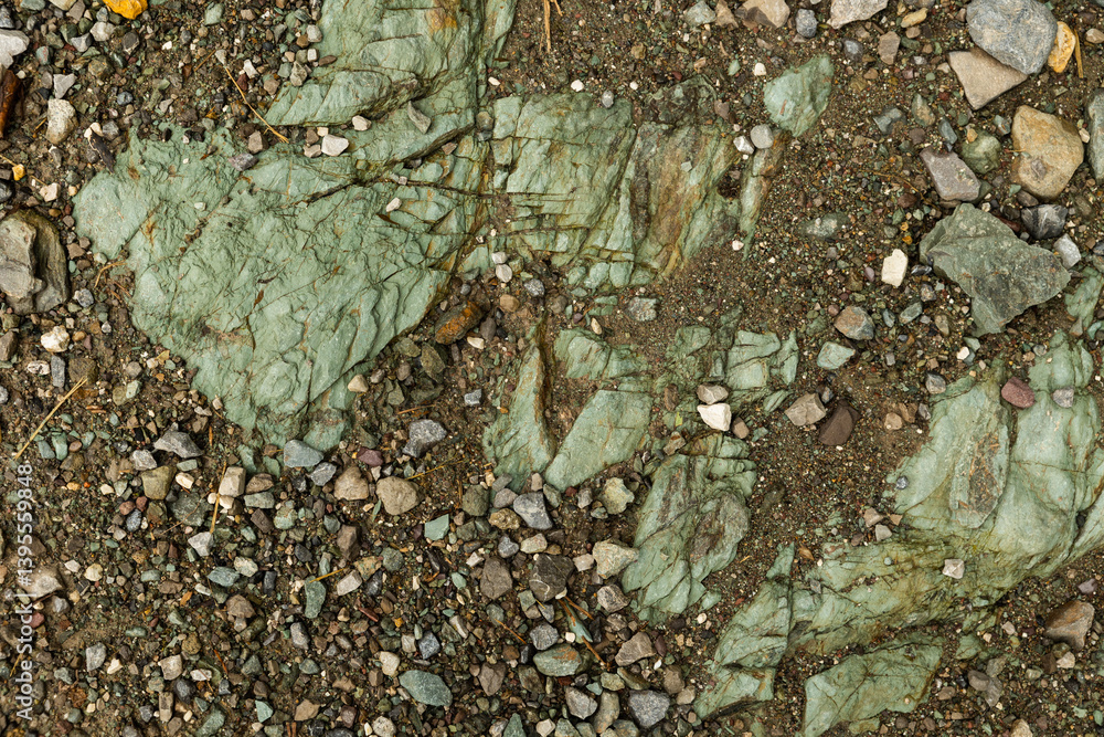 terreno di montagna composto da terra fangosa e morbida, di color marrone e rocce e sassi di varie dimensioni tra il verde smeraldo e l'azzurro sbiadito