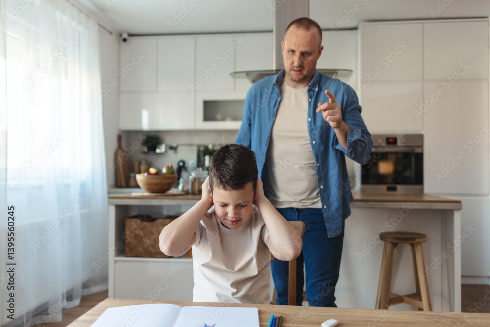 A shot of a little boy looking upset as his father talks in the background, covering ears with his hands. Nervous father shouting to his son after he seen that he didn't do his homework properly. A shot of a little boy looking upset as his father talks in the background, covering ears with his hands. Nervous father shouting to his son after he seen that he didn't do his homework properly.