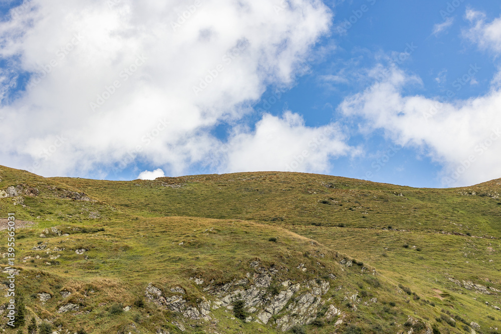 pendii e cime erbose in un ambiente naturale di montagna, di giorno, sotto un cielo parzialmente nuvoloso, nelle Alpi del nord Italia