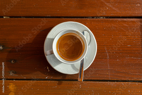 Obraz na płótnie tazza bianca piena di caffè espresso caldo, appoggiata su un piccolo piatto, con un cucchiaino, sopra un tavolo di legno, di girono, visto da sopra w salonie