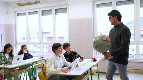 Geography instructor demonstrating world globe while engaging students in classroom learning environment, showcasing educational interaction and global knowledge exploration