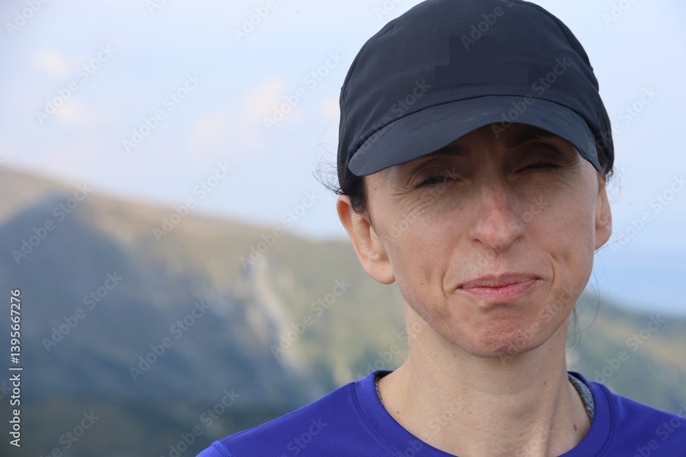 portrait of a female runner wearing a baseball cap and squinting in mountains portrait of a female runner wearing a baseball cap and squinting in mountains