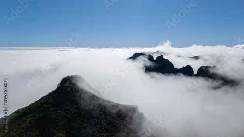 Among the Clouds, a Majestic Mountain Peak Emerges Under a Bright Blue Sky