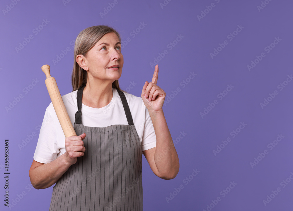 Woman with rolling pin pointing upwards on violet background Woman with rolling pin pointing upwards on violet background